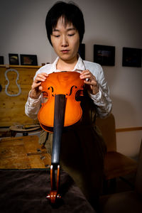 Young chinese woman violin maker checking the quality of her violin in the workshop