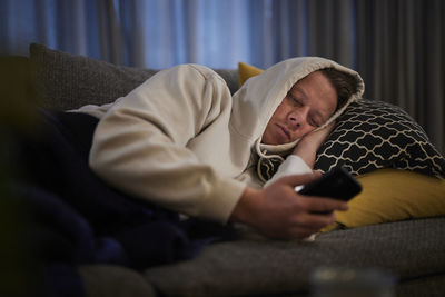 Ill man lying on sofa with smartphone