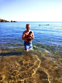 Full length of shirtless boy standing on beach against sky