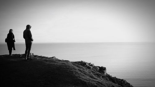 People standing on rock by sea against clear sky