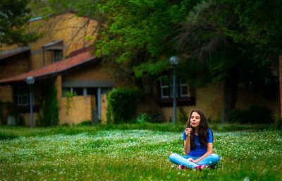 Teenage girl sitting on lawn while blowing dandelion