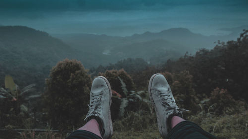 Low section of person relaxing on mountain against sky