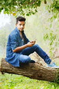 Portrait of young man sitting on tree