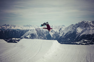 Snowboarder jumping against sky at mountain