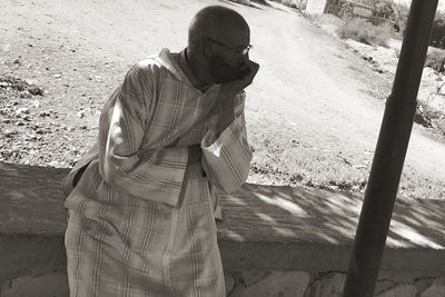 Side view of man holding camera while standing outdoors