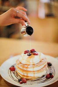 Close-up of hand pouring syrup over pancake