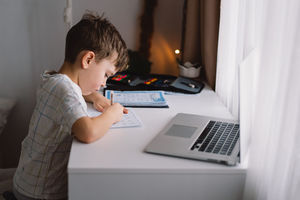 Cute kid boy studying at home with laptop and doing school homework.