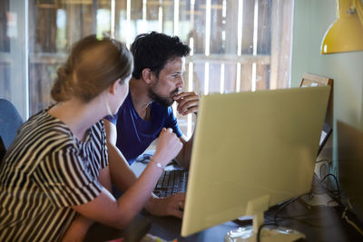Male and female colleagues discussing at computer desk in creative office