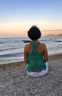 Rear view of woman siting on beach against clear sky