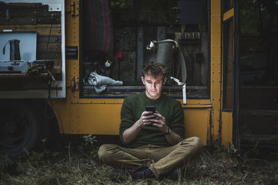 Man sitting cross-legged while using smart phone against motor home during camping