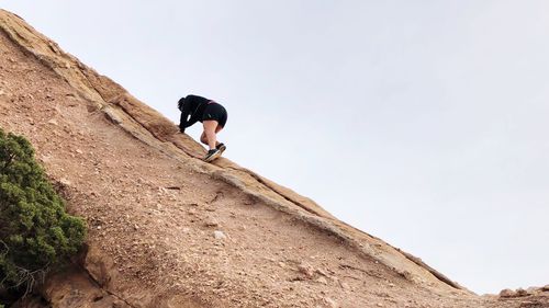 Low angle view of woman standing on cliff against clear sky