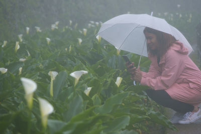 Woman photographing flowers while crouching during rainy season