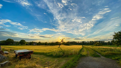 Empty road amidst field against sky during sunset