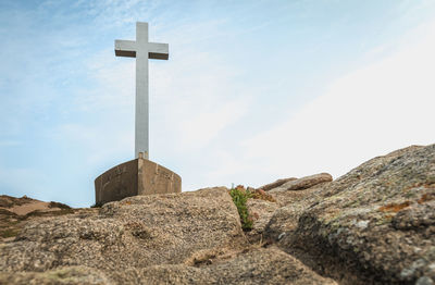 Low angle view of cross on rock against sky