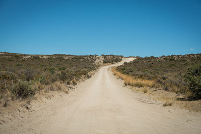Dirt road amidst landscape against clear blue sky