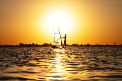Woman windsurfer silhouette at lake sunset. beautiful beach landscape. summer water sports