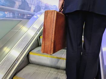 Midsection of businessman holding suitcase while standing on escalator