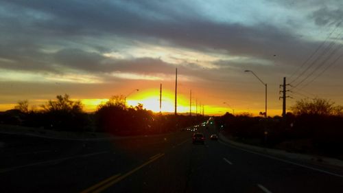 Cars on road against cloudy sky at sunset