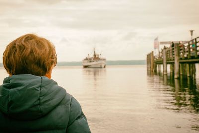 Rear view of boy looking at sea against sky during sunset
