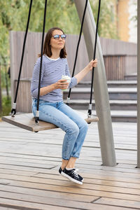 Full length of woman with coffee cup sitting on swing