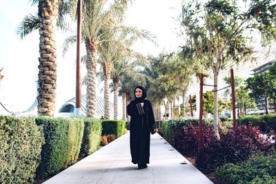 Portrait of young woman standing on footpath amidst trees