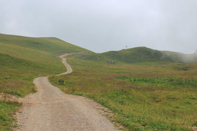 Dirt road amidst field against sky