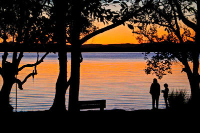 Silhouette people standing by lake against sky during sunset