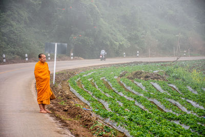 Monk standing on road by agriculture field