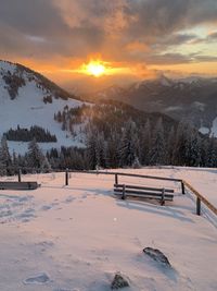 Snow covered field against sky during sunset