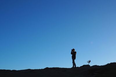 Young woman standing on land against clear blue sky