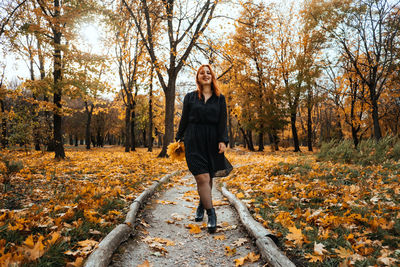 Outdoor autumn portrait of happy smiling plus size red hair woman in dress walking in fall park