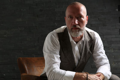 Portrait of mature businessman with beard sitting on chair against wall