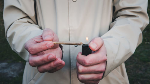 Midsection of man burning weed joint outdoors