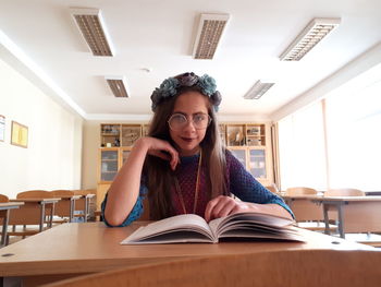 Portrait of student wearing wreath with book on table sitting in classroom