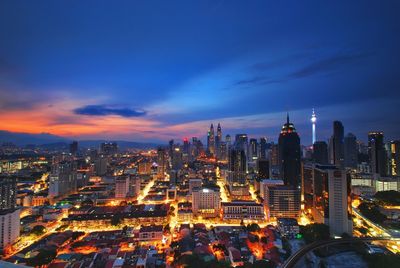 Illuminated buildings in city against cloudy sky