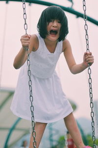 Portrait of girl screaming while standing on swing at playground during sunset