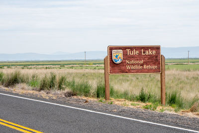 Information sign on road amidst field against sky