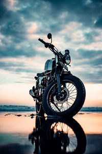 Surface level view of motorcycle at beach against sky during sunset