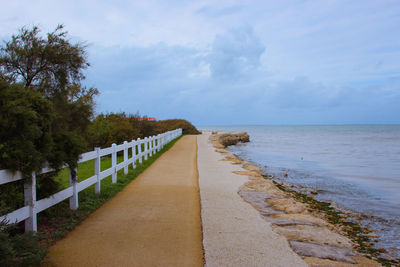 Footpath leading towards sea against sky