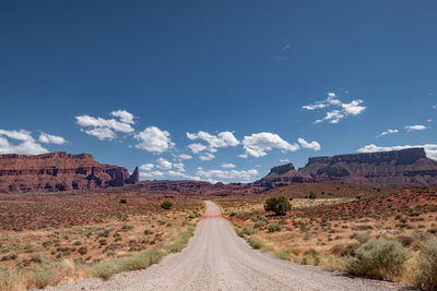 Dirt road amidst desert against sky