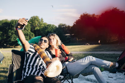 Friends taking selfie on smart phone while sitting with balloon in event