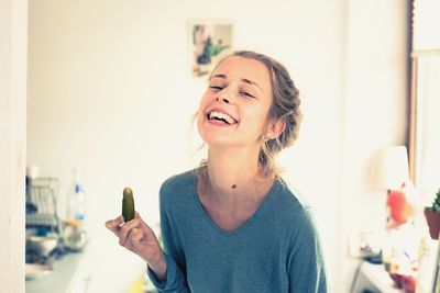 Portrait of happy young woman holding pickled cucumber at home