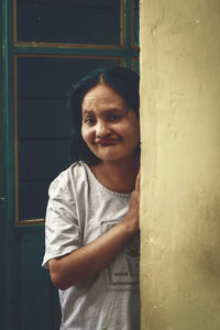 Portrait of smiling young woman standing against window