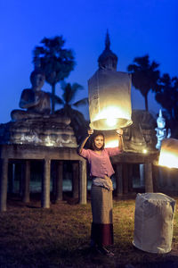 Full length portrait of young woman in temple against sky at night
