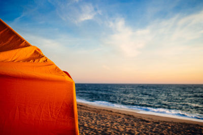 Cropped image of orange parasol at beach against sky during sunset