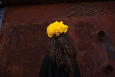 Close-up of woman wearing yellow flower against metallic wall