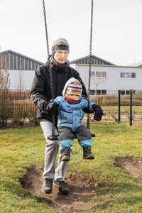 Full length man swinging granddaughter sitting on swing at park during winter