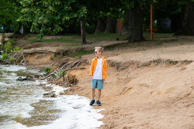 A boy in an orange shirt on the seashore. a child in sunglasses person