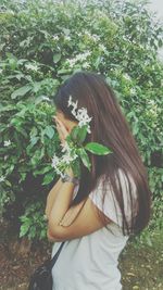 Young woman standing against green leaves