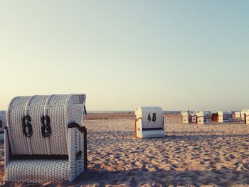 Hooded chairs on beach against clear sky